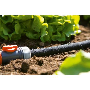Halli ja oranži värviga 15-meetrine Gardena tilkkastmissüsteemi voolik, mõeldud kasutamiseks maa sees asuvate roheliste taimede vahel.