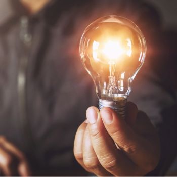 Inimese käes hõõguv elektripirn, mis toob esile inimmõõtmelise idee, valguse ja innovatsiooni sümboliseerimine.