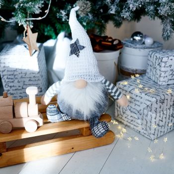 Kahe tekstiilist lumemehe kujuga dekoratsioon, millel on hallid ja valged mustrid ning puidust jalad ja nina, paigutatud koos puidust jõulukaunistuste ja kingitustega.