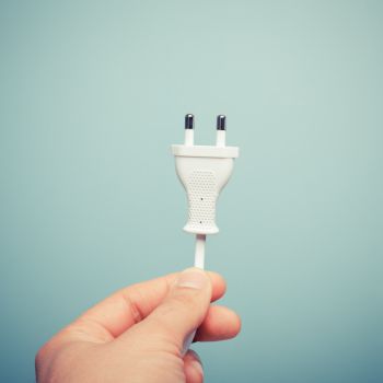 Valge kaheharulise pistikuga toitejuhe, mida hoitakse käes sinise tausta ees.