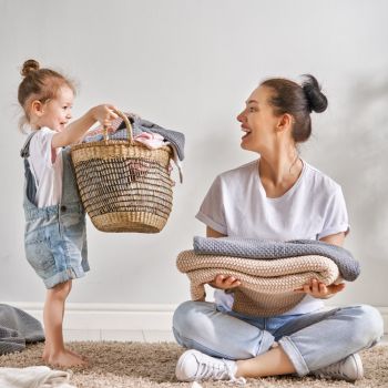Naine ja tüdruk istuvad vaibal, tüdruk hoiab korvi. Neil on seljas mugavad vabaajarõivad. Toas on minimalistlik ja hele kujundus.