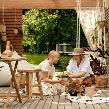 Kaks inimest istuvad terrassil, ümbritsetud lõõgastavate õuemööblite ja kodukaunistustega. Näha võib kauni rohelise maastiku taustal puhkenurka, kus on mugav diivan ja stiilne laud.