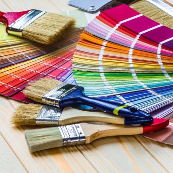 Valik värvipintslid puupinnal värvikaartidega. Näha on erineva suuruse ja harjastega pintslid, mis sobivad mitmekülgseteks värvimistöödeks.