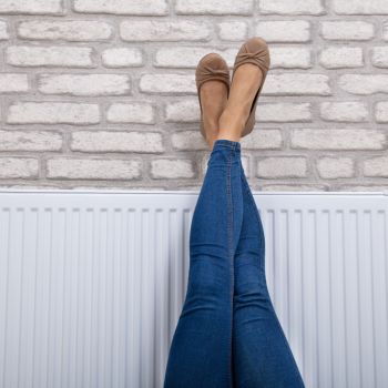 Naine kannab siniseid teksaseid ja pruune paeltega baleriina kingi, jalad sirutatud vastu telliskiviseina tausta.