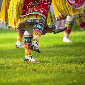 Kirjud traditsioonilised rahvarõivad ja käsitööga kaunistatud sokid kõnnivad rohul. Erksates toonides kollane, punane ja roheline domineerivad.