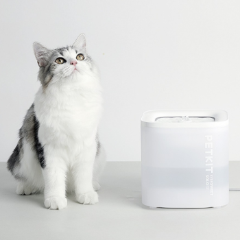 Valge ja läbipaistev plastist ruudukujuline seade kirjaga PETKIT paikneb laual halli-valge kassiga kõrvuti.