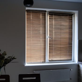 Klassikalise disainiga aknakate, mis koosneb kahest puidumustriga ruloost ja valgest raamist. Rulood on allalastud ja suletud asendis, blokeerides osaliselt valguse.