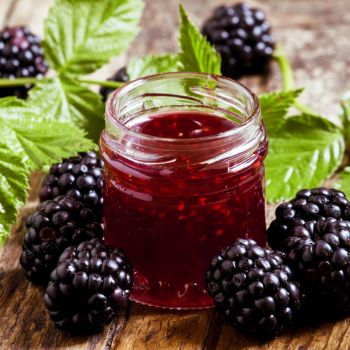 Klaaspurk täis ploompunast vaarikamoosi, ümbritsetud värske vaarikatega puidust laual.