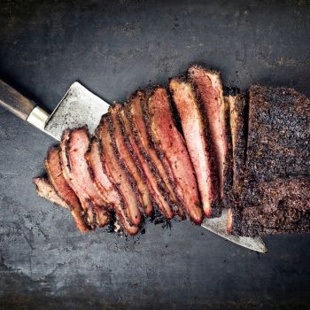 Lõigatud suitsuliha metallvardas, rikkaliku maitsekamaraga, mahlane ja kergelt süsimustaks küpsenud servadega.