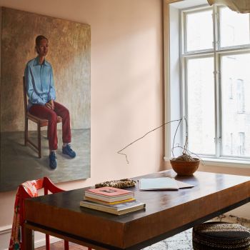 Ruumis on keskse elemendina suur laud, millel on mitu raamatut ja kauss. Akna juures ripub minimalistlik lamp, taustal on suur portreemaal.