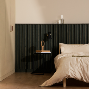 Kaasaegse disainiga magamistuba, millel on suur voodi ja beež voodipesu. Taustal on tume roheline seinaelement ja puidust öökapp koos lambiga.