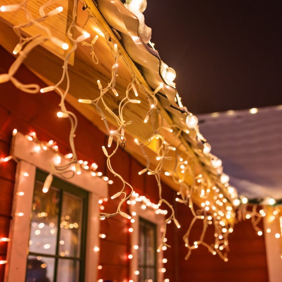 Valged ja värvilised jõulutuled ripuvad punase maja katusel ja akende ümber, luues piduliku atmosfääri.