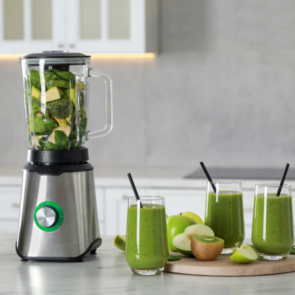 Roostevabast terasest korpusega blender, millel on läbipaistev klaasist kann, täidetud roheliste koostisosadega. Esipaneelil on roheline kraaniga juhtnupp. Taustal on kolm rohelist smuutit klaasides ja puuviljad.