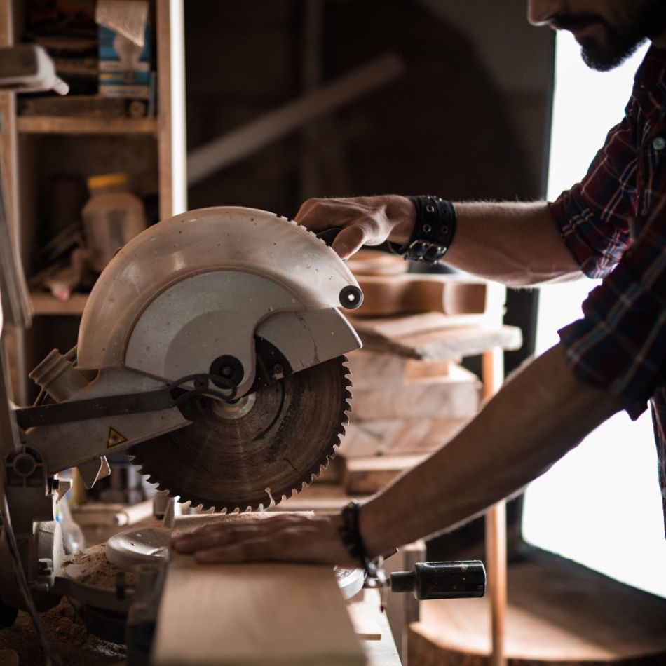 Mees kasutab töökojas suurt elektrilist ketassaagi puidu lõikamiseks, keskendudes detailidele.