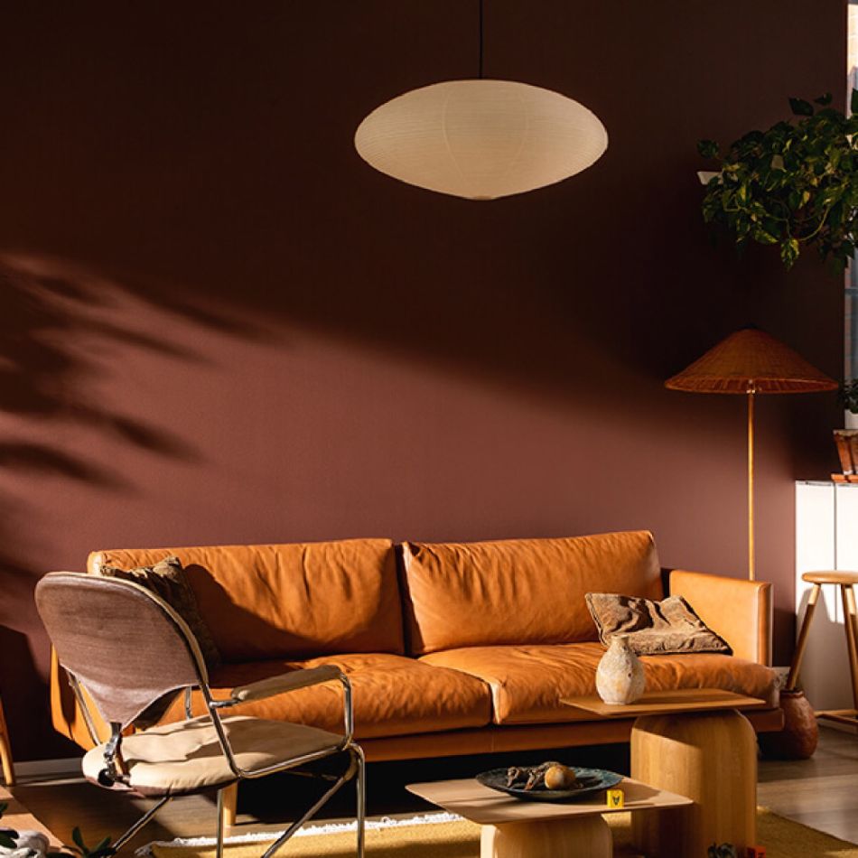 Kaasaegne elutuba, kus on pruun diivan, täiendav istekoht ja soe valgustus, luues mugava ja kutsuva atmosfääri.