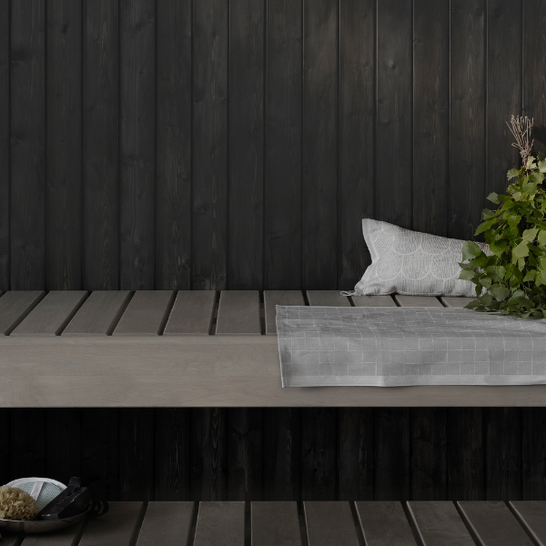 Puidust saunalava koos halli padja ja dekoratiivsete taimedega, taustal must puitsein.