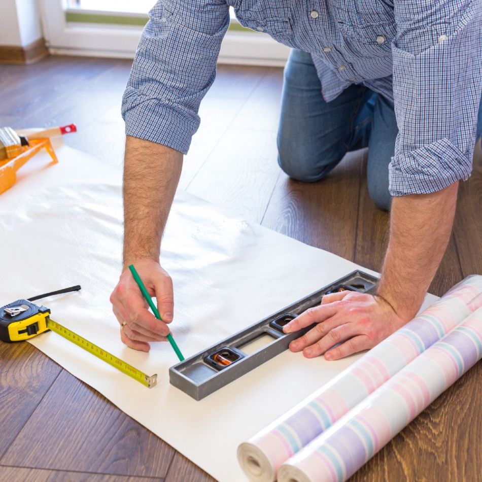 Meesterahvas märgib paberit ja kasutab tasapinnatöövahendit tapeedi paigaldamiseks.