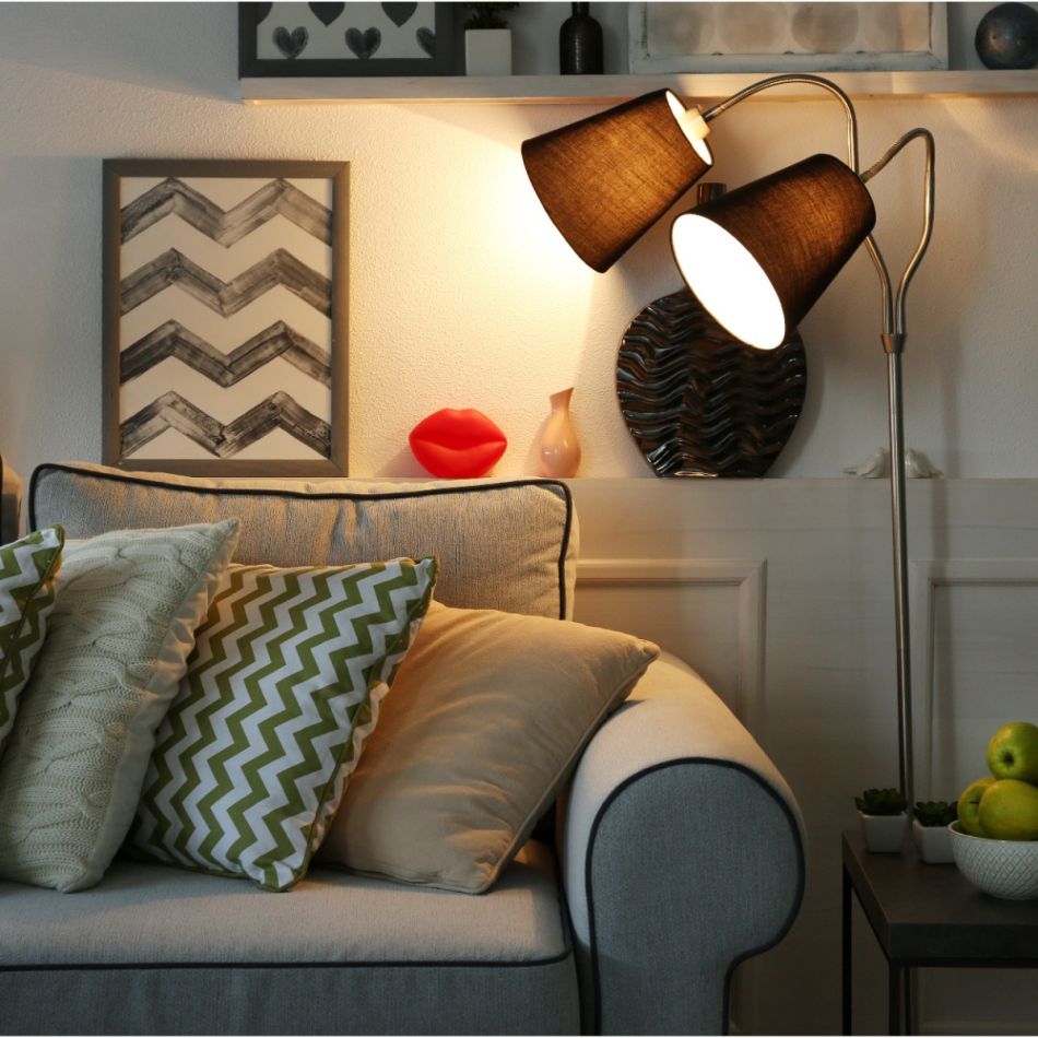 Stiilne diivaninurk, millel on hall tugi ja mitmevärvilised padjad. Seina külge kinnitatud reguleeritav kahe lambivarjuga valgusti valgustab ruumi efektiivselt.