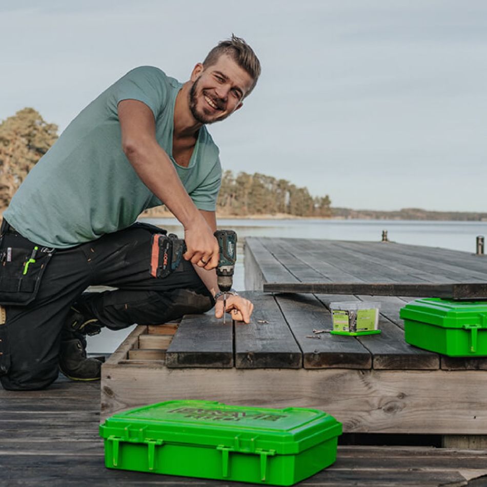 Mees paigaldab terrassile paneeli, rohelised tööriistakohvrid käepärast.