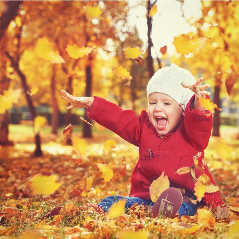 Väikelaps naudib sügislehti, istudes rohtunud pinnal puistatud kollaste lehtedega. Kannab punast jakki ja valget mütsi.