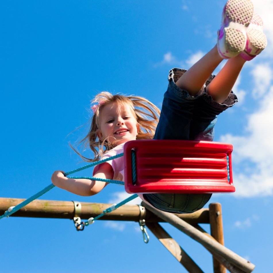Väike tüdruk mängib õues, kiikudes punases korvis ühe jalaga suunaga ülespoole. Ta kannab roosat pluusi ja lühikesi pükse, tagaplaanil sinine taevas ja pilved.