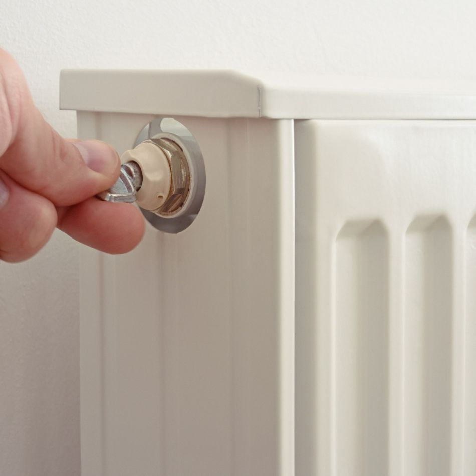 Isiku käsi keerab radiaatori termostaadi nuppu, mis on kinnitatud valge radiaatori külge.