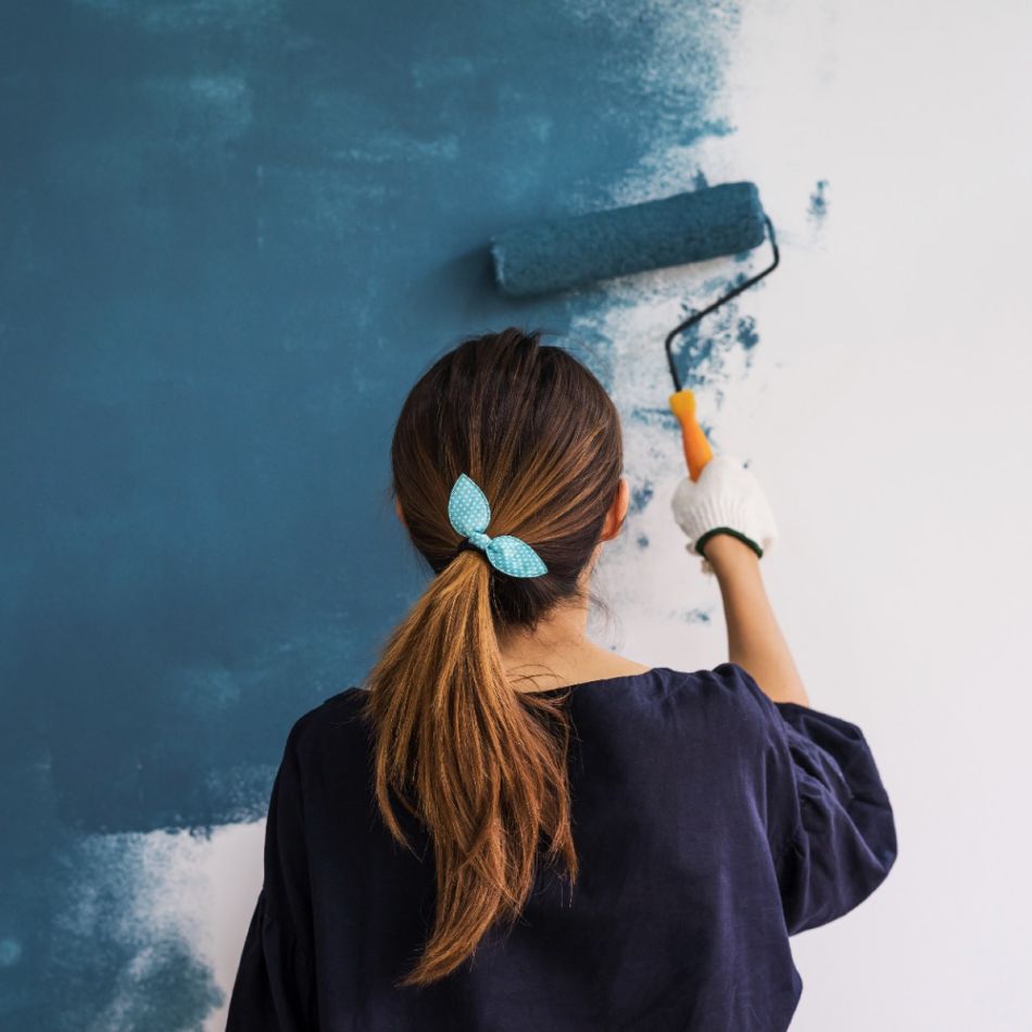 Naine värvib sinist seina suure sinise rulliga, kandes tumedat üleriideid ja juukseid kinni hoidvat juuksekummi.