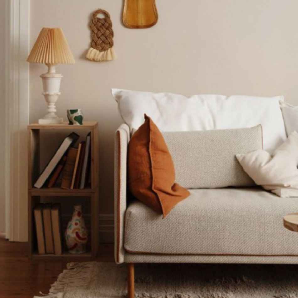 Kaasaegne sisustuspilt, kus on beež diivan valgete ja pruunide patjadega, puidust külglaud ja põrandalamp. Taustal seinil valge tooniga dekoratiivesemed.