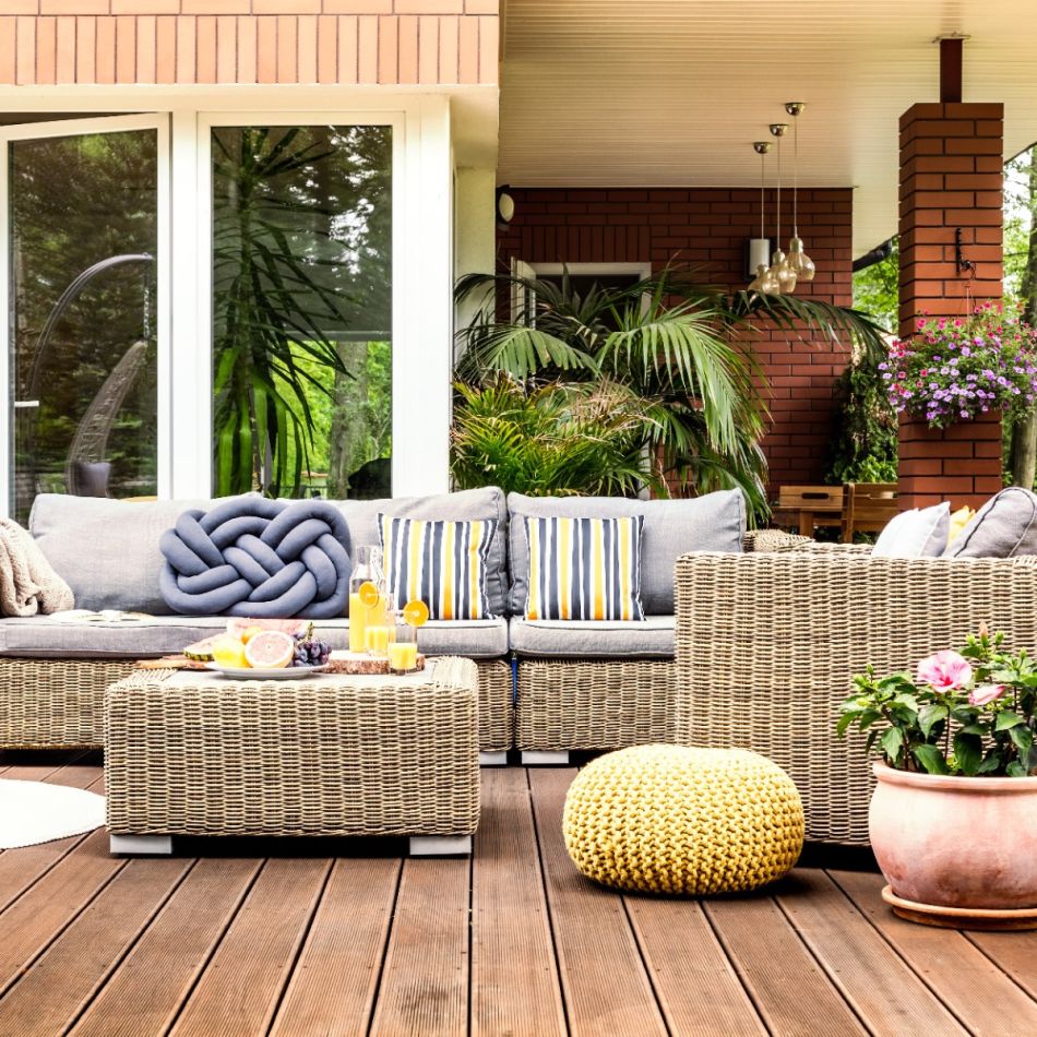 Välimööblikomplekt terrassile, sisaldab beeži värvi rotangist diivanit, kahte tugitooli ja kollast pallikujulist istet. Lisaks on pildil puitpõrand ja elutaimed.