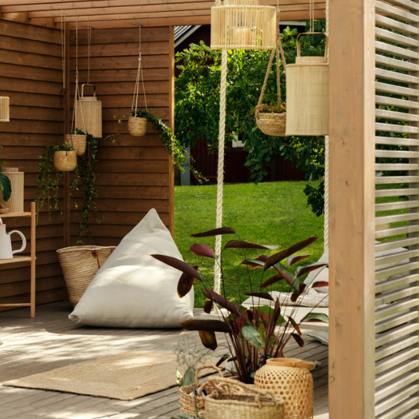 Terrassiga aed, kus on puitpõrand, valge suur padjaga istumisnurk ja rippuvad taimed. Stiilne ja looduslähedane välisilm kuulub 2024. aasta terrassitrendide hulka.