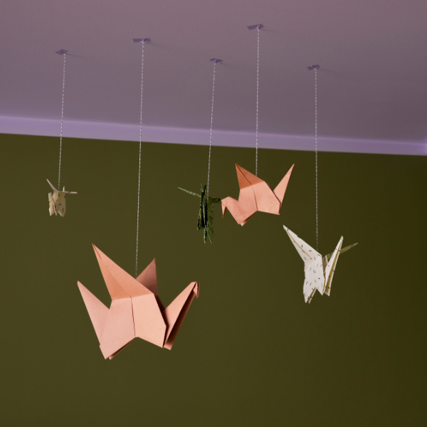 Lakke kinnitatud rippuvad paberlinnud erinevates suurustes ja värvitoonides, taustal oliivroheline sein ja helelilla lagi.