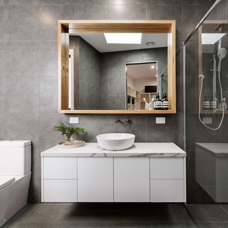 Kaasaegse disainiga vannituba, millel on suur peegliga seinakapp, valge kraanikauss valgel aluskapil ja hallid seinad.